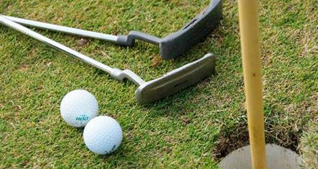 Close up photo of two putting sticks and two golf balls beside putting hole and flag at Seapark