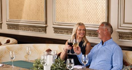 Female and male sitting in the gallery of the old inn cheering with wine glasses