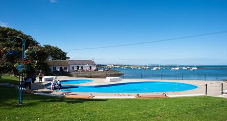 A photo of Cockle Row Cottages taken from a distance to include the seasonal paddling pool in shot on a bright sunny day
