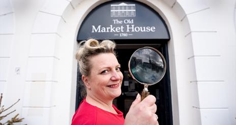 Miss Scarlett holds a magnifying glass at the doorway of The Old Market House, Bangor