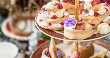 Elegant three-tiered cake stand filled with artisanal pastries, fruit tarts, and floral-decorated sweets, set against a softly blurred background with