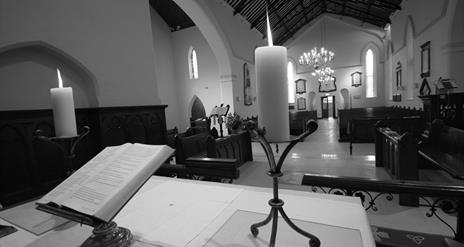 Black and white photo of from the alter of the church showing the Bible and lit candlesticks overlooking the pews