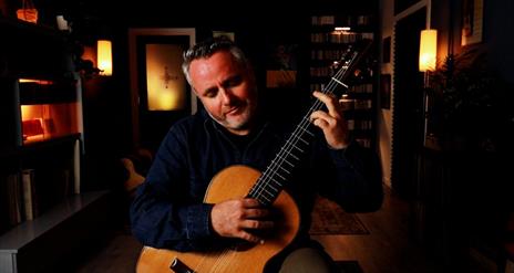 Guitarist Matthew McAllister playing guitar in a small dark room with some mood lighting.