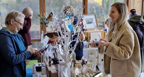 A craft stall at a North Down Craft Collective Fair at WWT Castle Espie.  A visitor is chatting to a local artist.