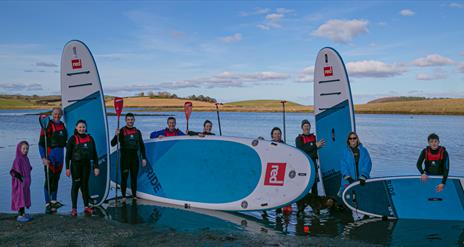 Paddleboarders of all ages standing with boards and paddles back from a session on the waters of Ballymoran Bay