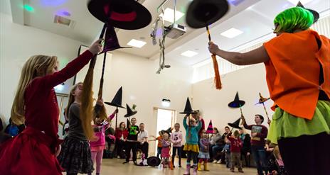 Children holding up witches hats and brooms, dressed for Hallowe'en