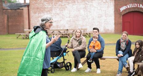 A lady dressed in a green cloak telling stories to children in the ulster folk museum