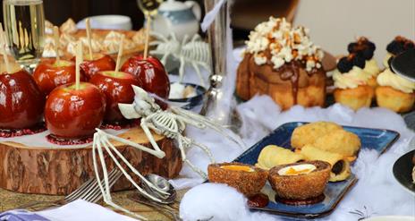 Table set up with food including toffee apples, scotch eggs, sausage rolls, cake and cupcakes with halloween decor