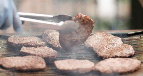 hand turning a burger on the bbq with a blue glove on it