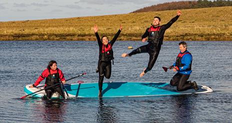 Four paddleboarders sharing a board, two of them jumping into the water