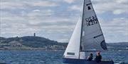 A small sailing dinghy with two people onboard, sailing on open water