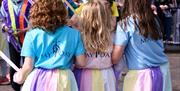 Trio of girls taking part in the annual maypole dancing dressed in pastel skirts to match the ribbons of the Maypole