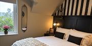 Double bedroom with a white bed, black headboard, bedside lighting and window view.