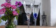Two glasses of fizz with a vase of flowers and a cork, on a table