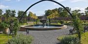 a photograph of the water fountain in the bangor walled garden shot through a metal sculpture
