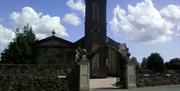 Photo of the Church from the car park, showing the entrance gates and arch way leading to the front doors of the church