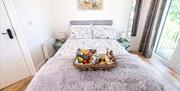 Double Bed with food hamper basket with local produce placed on the bed. Patio doors leading to outside area.