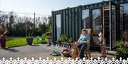 Christine of Kiri Cottage Crafts sitting outside of her workshop in front of a spinning wheel