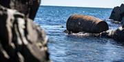 An image of a distillery barrel floating in the water beside the rocks