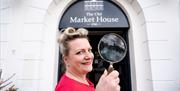 Miss Scarlett holds a magnifying glass at the doorway of The Old Market House, Bangor