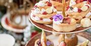 Elegant three-tiered cake stand filled with artisanal pastries, fruit tarts, and floral-decorated sweets, set against a softly blurred background with