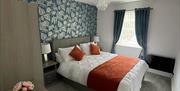 This is the master bedroom consisting of a set of drawers with a 3 door wardrobe bedisde tables in between a kingsize bed beside the window and radiat