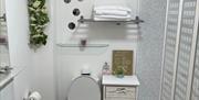 White bathroom suite sink on the left with shel and mirror. Black and white flooring deep burgundy bathroom mat set.  Folding shower screen with elect