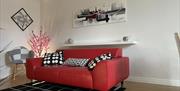 Red leather settee with black and white checked rug on a wooden floor showing  black/red/white abstract picture on wall above.
Black and white chair a