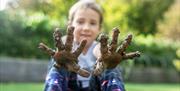 A child holding muddy hands up to the camera.
