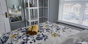 Double bedroom at rear of property with large wall mirror and white unit for storage. Colours are blues/greys/yellows