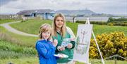 Painting outside with a canvas on an easel using Quentin Blakes illustration as inspiration, in the grounds of WWT Castle Espie
