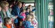 group of adults and children inside viewing room looking out of window.