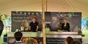 Image of a man and woman behind a demo kitchen talking to audience