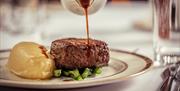 Gravy being poured over a plated steak