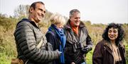 A group of 4 adults smiling and laughing as they walk through wetlands.