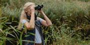 A woman looking through binoculars in a wetlands.