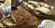 A photo of fresh baked cake and soda bread on the table with tea cups, curled butter and jam ready for eating