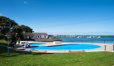 A photo of Cockle Row Cottages taken from a distance to include the seasonal paddling pool in shot on a bright sunny day
