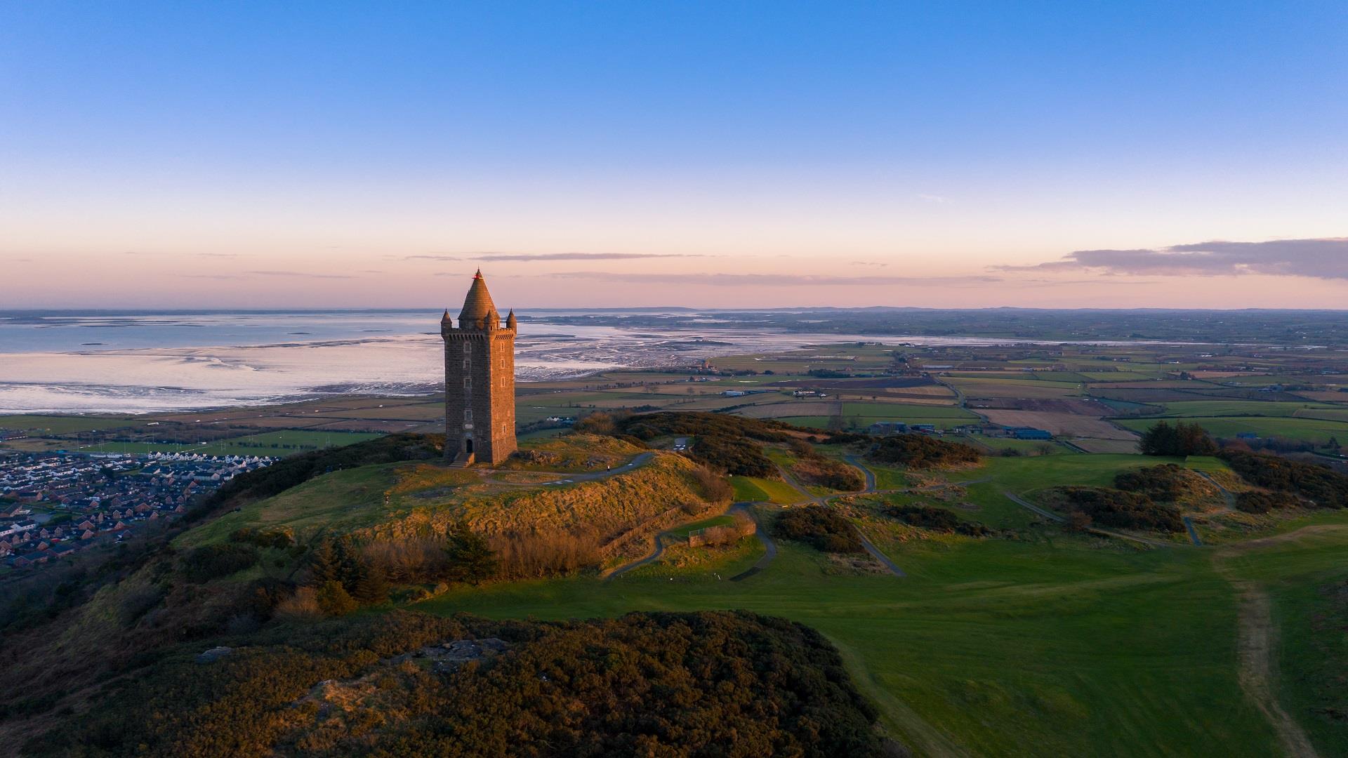 An image of Scrabo Tower at sunset with the wash of Strangford Lough in the background, Newtownards town and the surrounding landscapes and drumlins