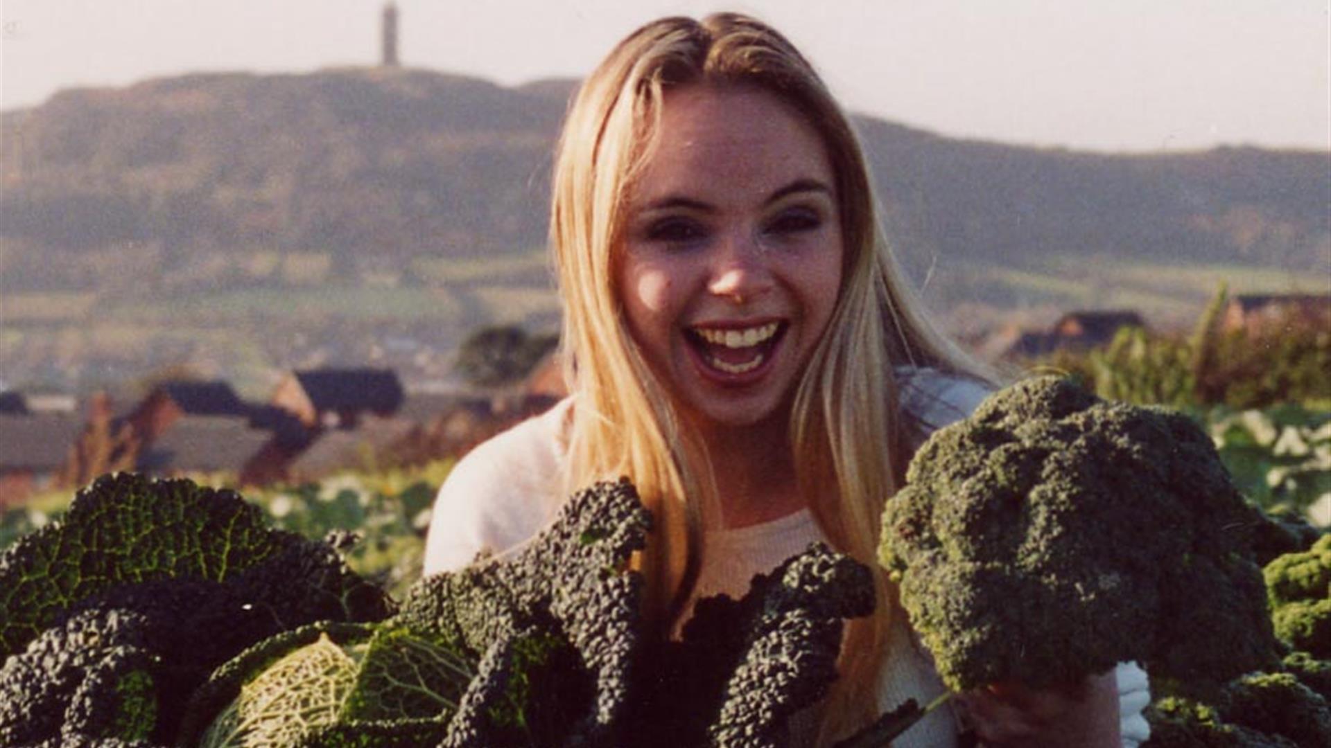 Photo of a woman holding freshly pulled vegetables with Scrabo in backdrop