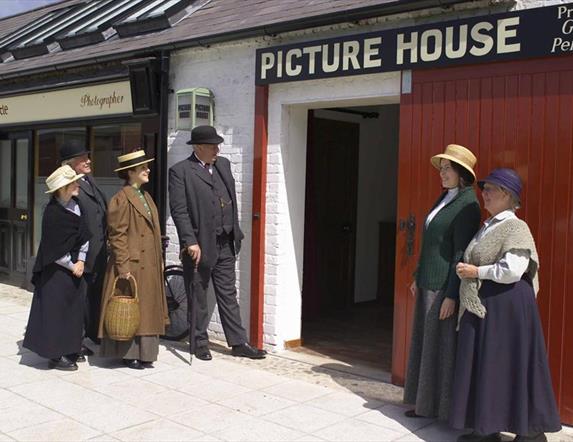 Image of a group of ladies and gents dressed in old fashioned clothing visiting the on site Picture House