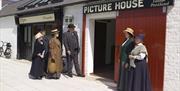 Image of a group of ladies and gents dressed in old fashioned clothing visiting the on site Picture House