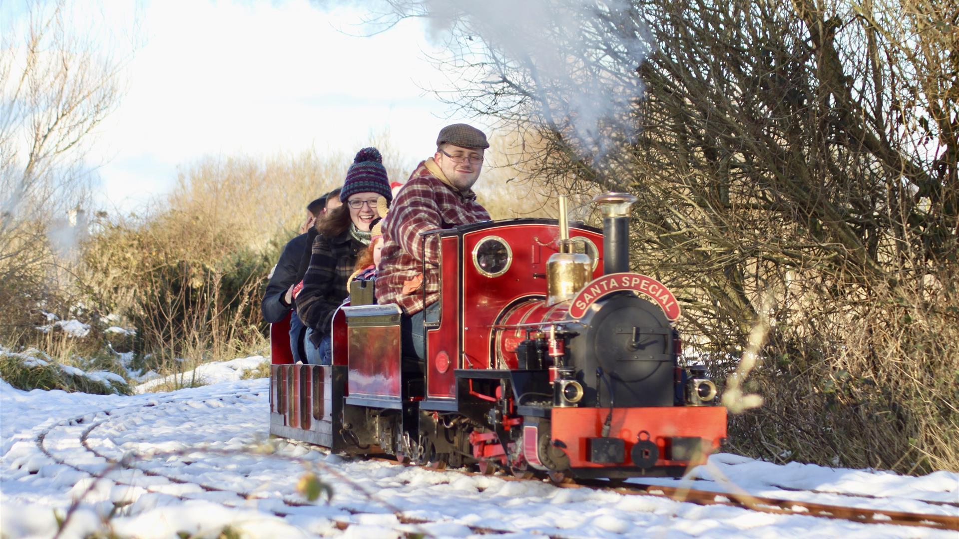 a photo of a group of adults on a small train surrounded by snow and trees