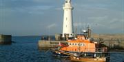 A photograph of Donaghadee lifeboat orange in colour moored in the water in front of donaghadee lighthouse
