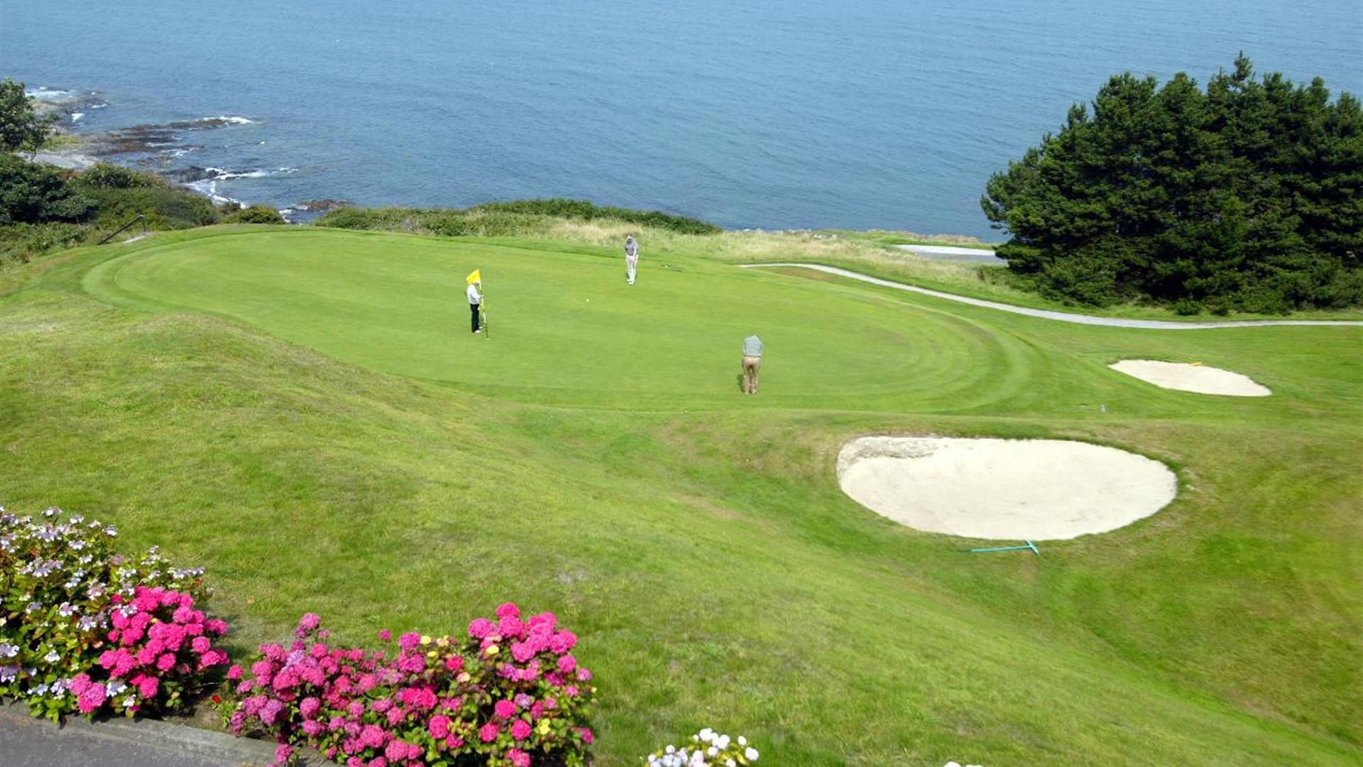 Photo of golfers in play on the green with waters of Belfast Lough in background
