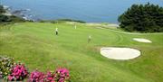 Photo of golfers in play on the green with waters of Belfast Lough in background