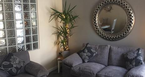 a photo showing a living room with sofas, a mirror, a plant and a window