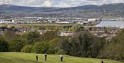 Golfers on the green with woodland and Belfast city in the background