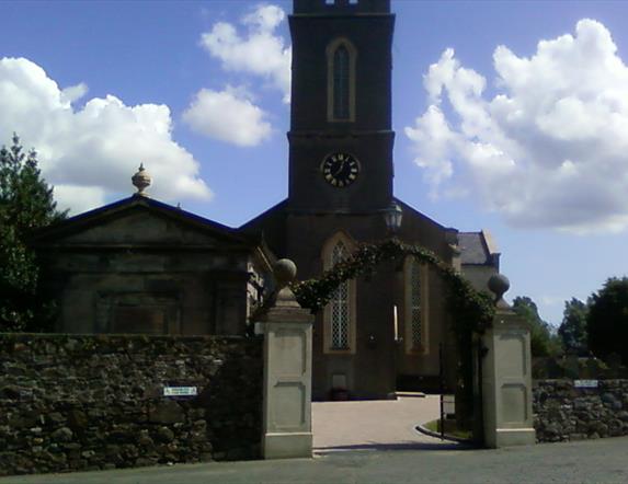 Photo of the Church from the car park, showing the entrance gates and arch way leading to the front doors of the church