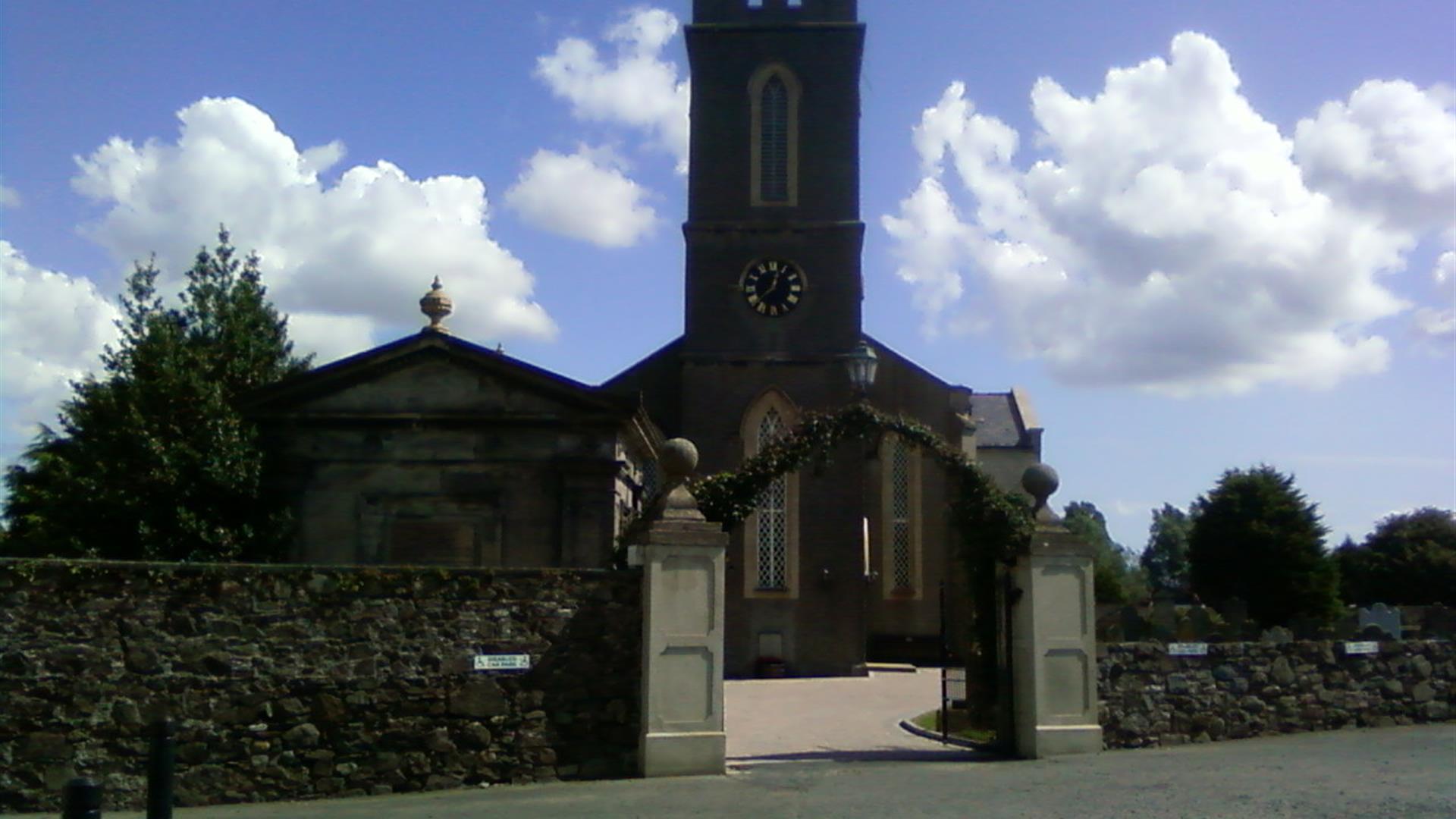 Photo of the Church from the car park, showing the entrance gates and arch way leading to the front doors of the church